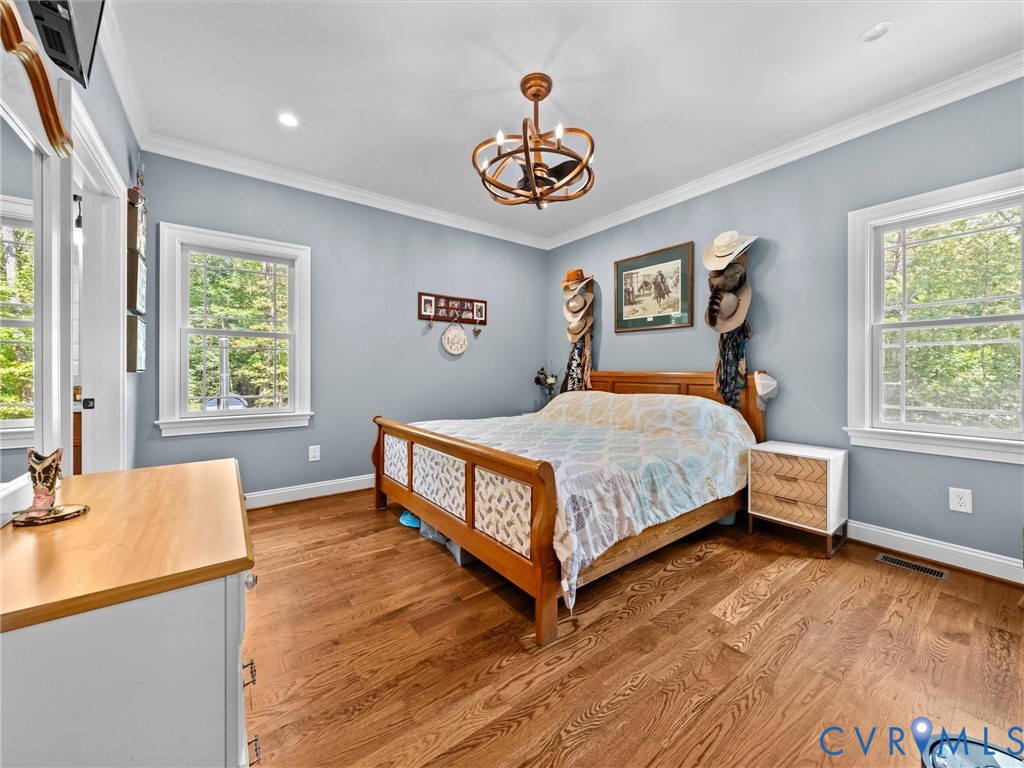 Another view of the spacious first-level primary bedroom highlights the beautiful hardwood floors, elegant tray ceiling, and abundant natural light. A peaceful retreat with two closets and a private en-suite bath!