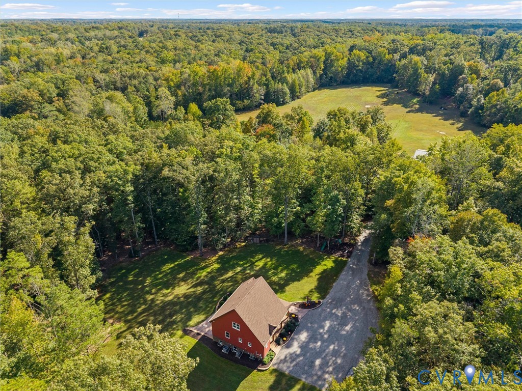 A stunning aerial perspective of The Little Red Homestead showcases the beautiful custom-built home nestled among mature trees, with a picturesque driveway winding through the property. Surrounded by rolling pastures and lush woodlands, this peaceful setting offers exceptional privacy, natural beauty, and the charm of country living!