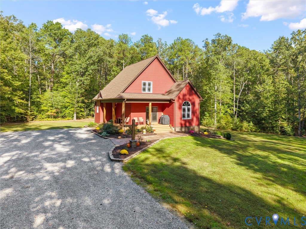 A welcoming approach to The Little Red Homestead showcases the charming covered front porch with beautiful white oak posts, attractive landscaping, and ample gravel parking. Surrounded by mature trees, this picturesque setting offers both convenience and country charm!