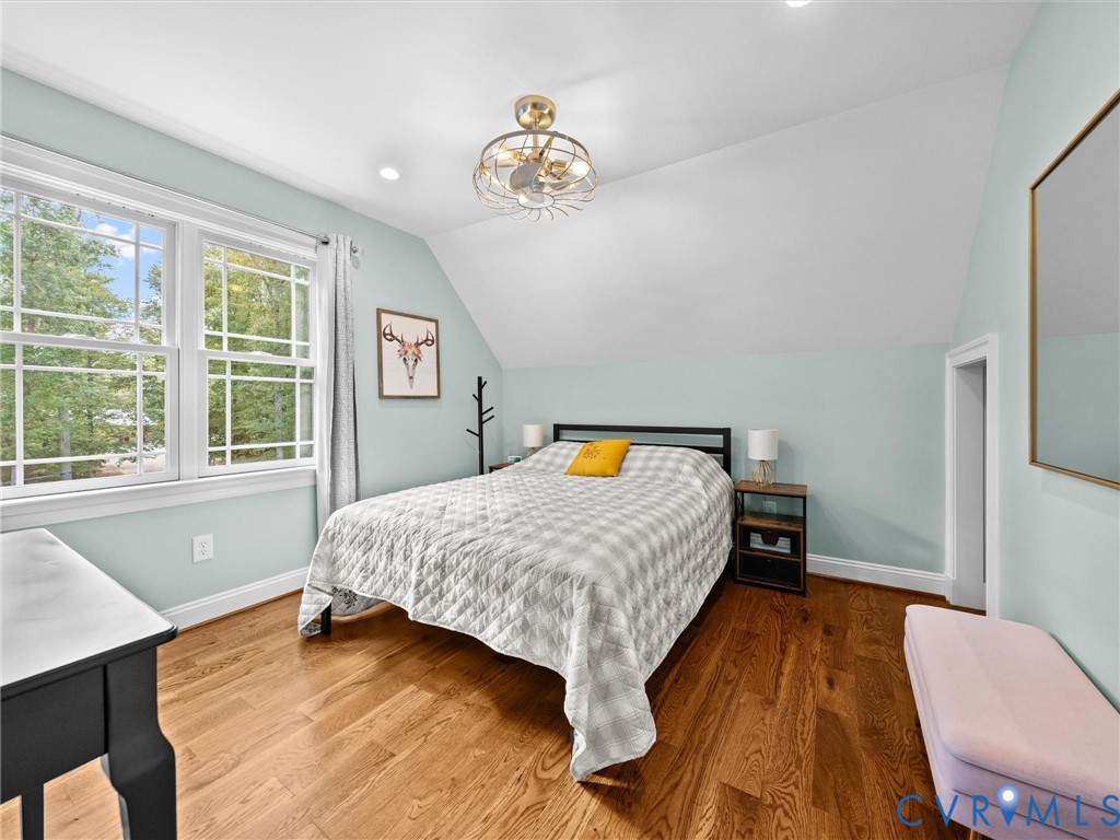 This spacious upper-level bedroom features beautiful hardwood floors, a ceiling fan, a generous walk-in closet, and large windows that fill the room with natural light while offering peaceful views of the surrounding countryside.
