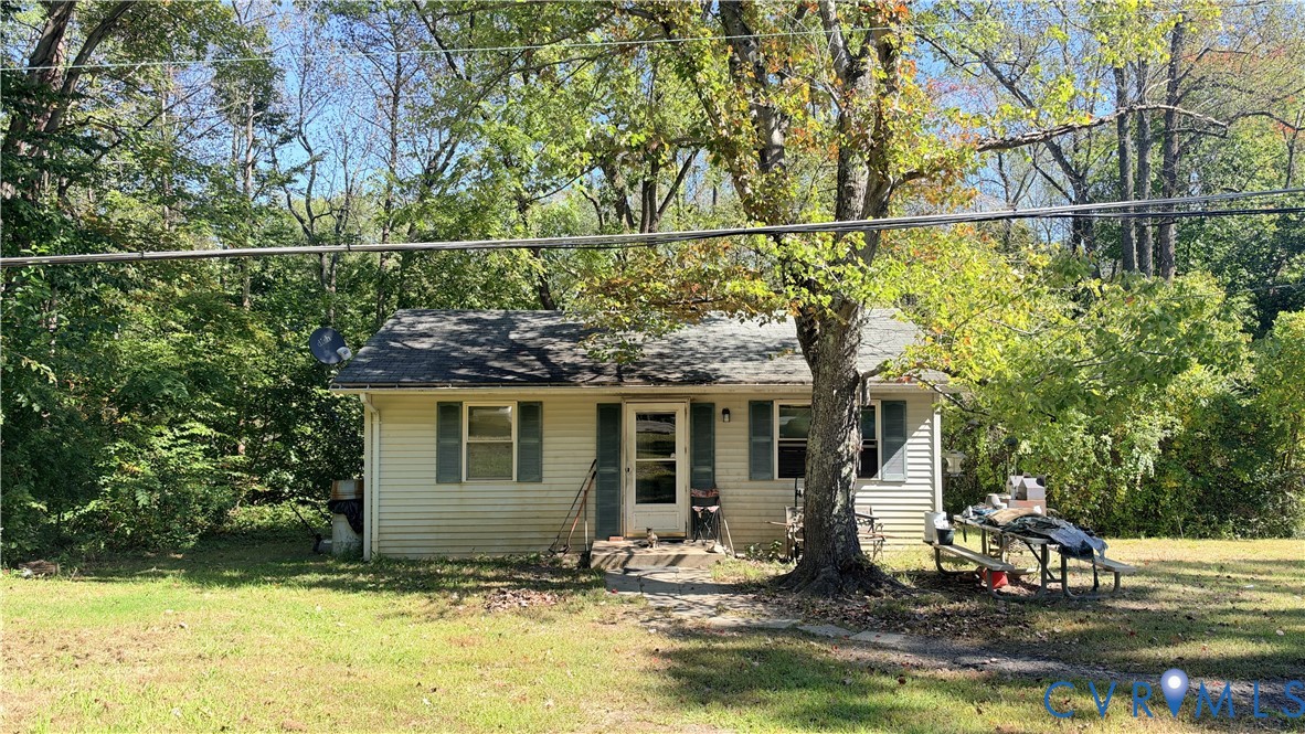 Single-story residence featuring horizontal vinyl siding, a gabled roof, shuttered windows, and mature surrounding trees