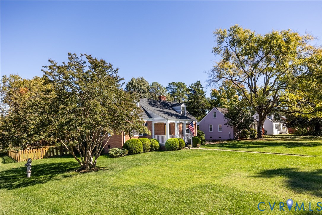 Brick exterior residence featuring a covered front porch, gabled roofline, mature trees, and expansive lawn area Brick exterior residence featuring a covered front porch, gabled roofline, mature trees, and expansive lawn area