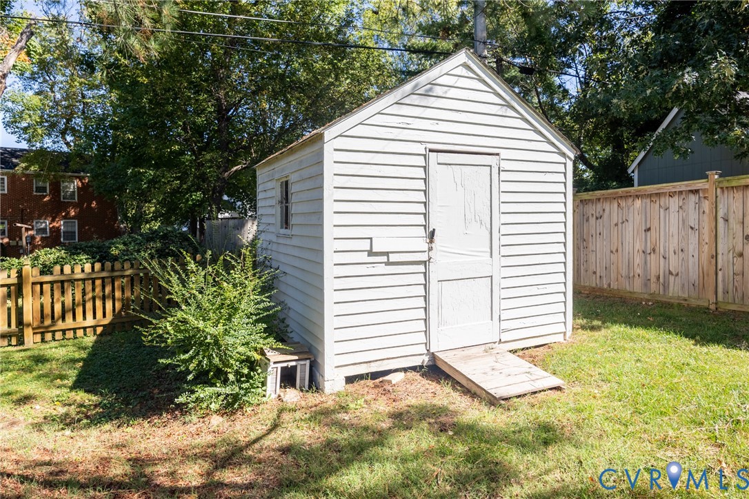 Storage structure with white horizontal siding, gabled roofline, single-panel entry door, and wooden ramp