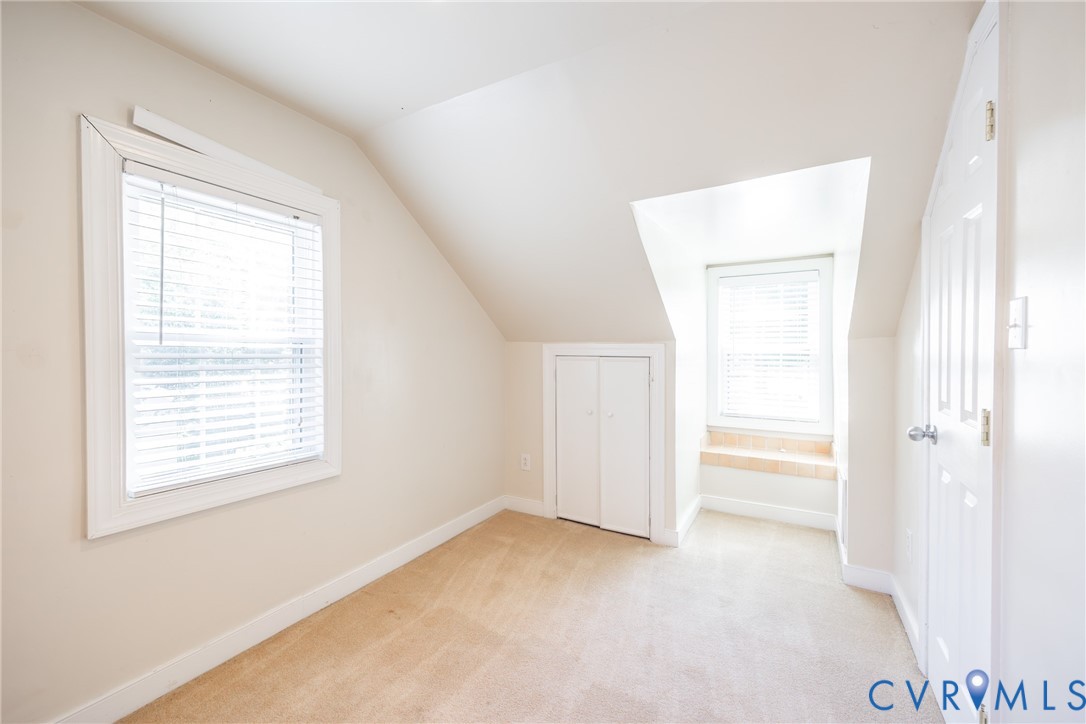 Interior space featuring vaulted ceilings, carpeted flooring, built-in storage cabinetry, a recessed window nook, and dual windows
