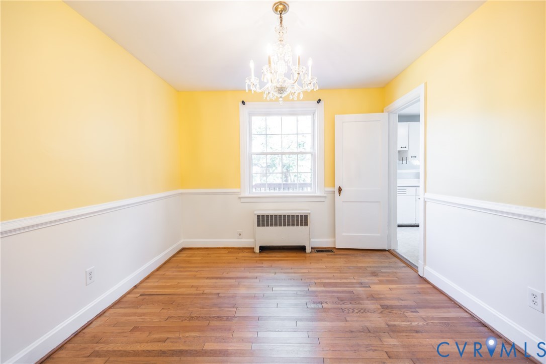 Room featuring wood-finish flooring, a multi-pane window, and a central crystal chandelier Room featuring wood-finish flooring, a multi-pane window, and a central crystal chandelier