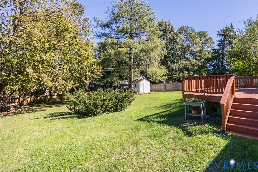 Spacious backyard featuring a wood deck with stairs, mature trees, a detached storage shed, and perimeter wood fencing