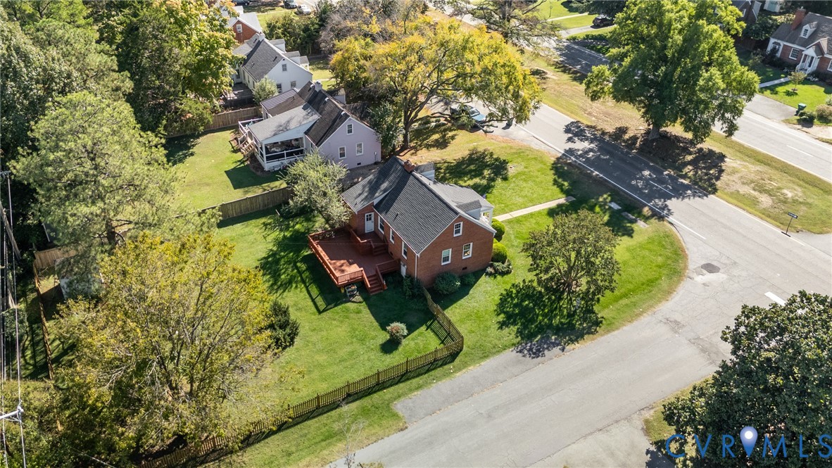 Brick exterior residence featuring an elevated wood deck, shingle roofing, and a fenced yard with mature trees