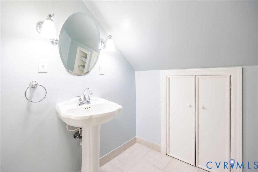 White pedestal sink with chrome faucet, oval wall-mounted mirror, dual globe wall sconces, and built-in under-eave storage cabinetry
