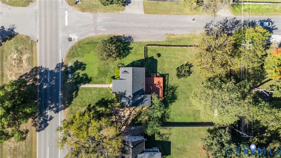 Aerial perspective of a corner lot featuring a dark shingle roof, integrated deck, and fenced grounds with mature trees