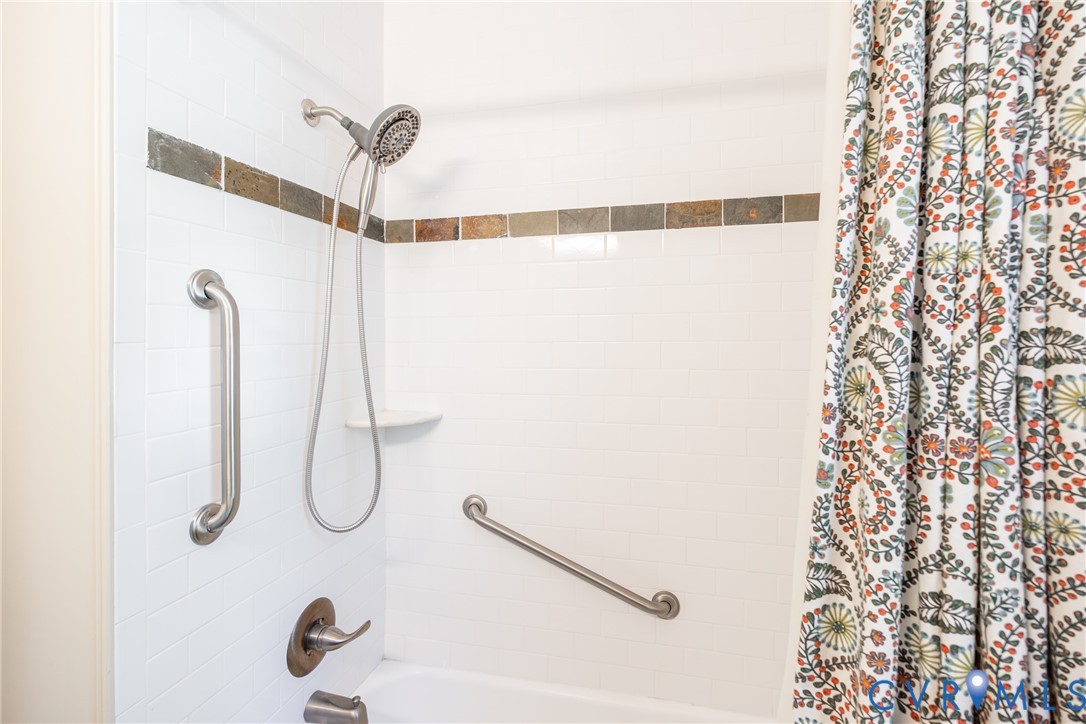 Bathtub surround featuring white subway tile, multi-tonal stone accent inlay, brushed metal plumbing fixtures, and integrated wall-mounted grab bars