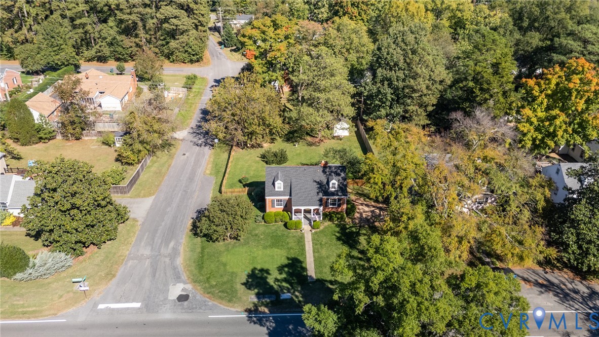 Aerial perspective of a detached residence featuring a brick facade, dormer windows, a pitched roof, and a mature tree-lined lot