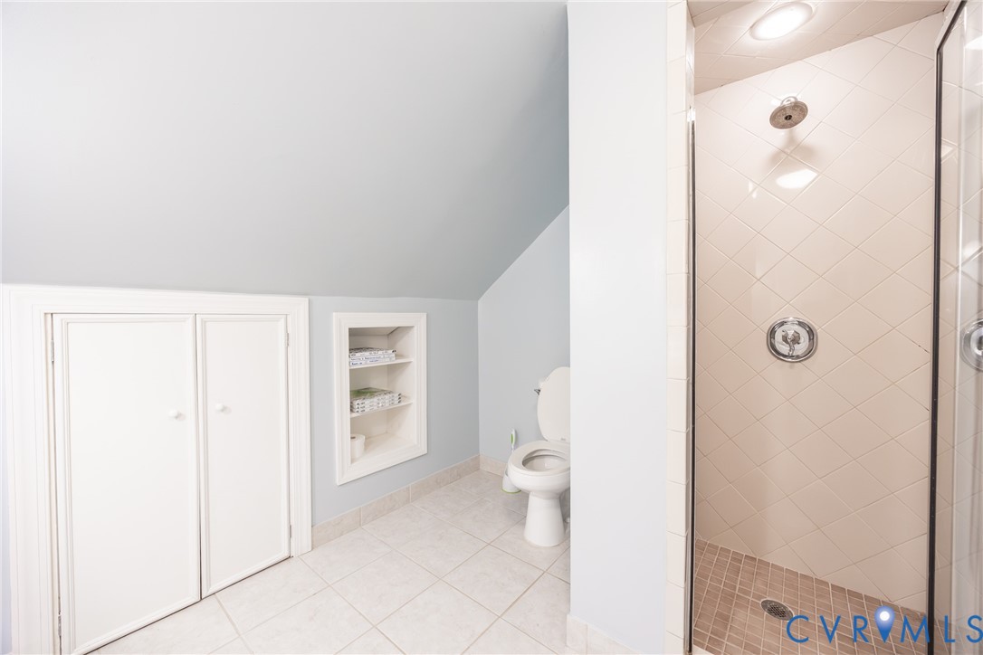 Bathroom featuring a walk-in shower with diamond-patterned wall tile, built-in recessed shelving, dual-door storage cabinetry, and tile flooring