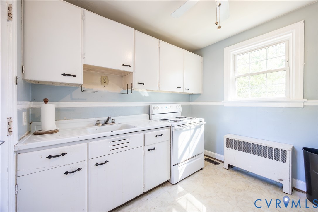 Kitchen featuring white cabinetry with dark hardware, a surface-mounted sink, a free-standing electric range, and a window with mullions