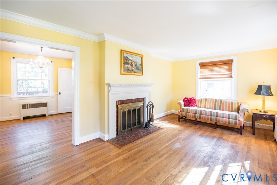Living area featuring hardwood flooring, a fireplace with a decorative mantel, crown molding, and multi-pane windows Living area featuring hardwood flooring, a fireplace with a decorative mantel, crown molding, and multi-pane windows