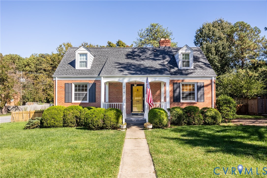 Brick exterior Cape Cod style home featuring a covered front porch, dual dormer windows, gable roof, and shuttered windows