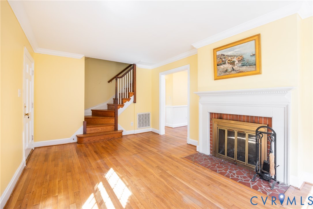 Fireplace with a brick hearth and white mantel, wood-finish flooring, and a staircase featuring a wooden handrail and balusters Fireplace with a brick hearth and white mantel, wood-finish flooring, and a staircase featuring a wooden handrail and balusters