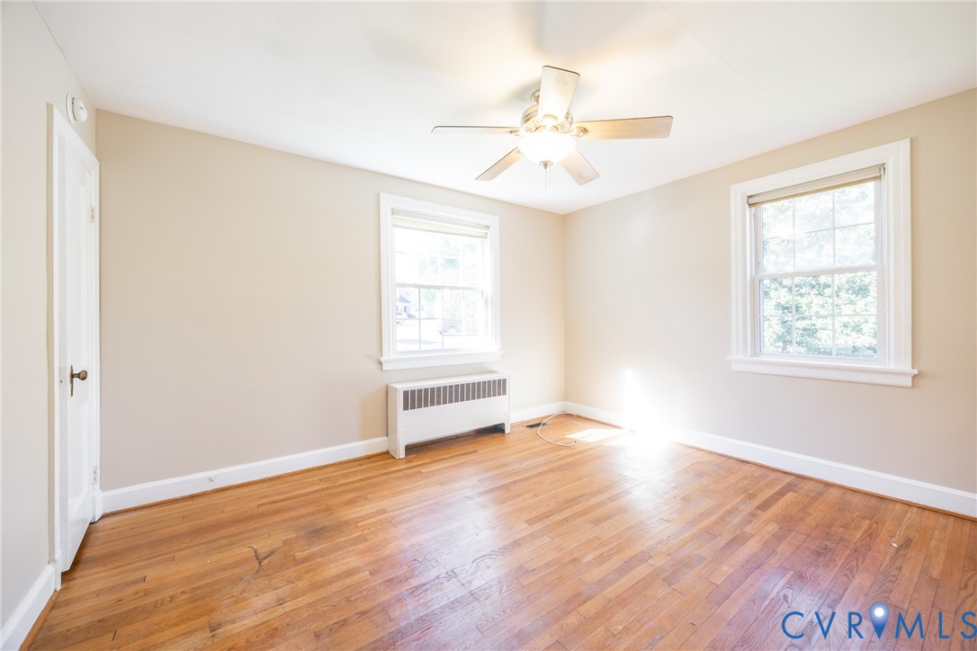 Room featuring wood-finish flooring, two multi-pane windows, and a central ceiling fan with integrated lighting