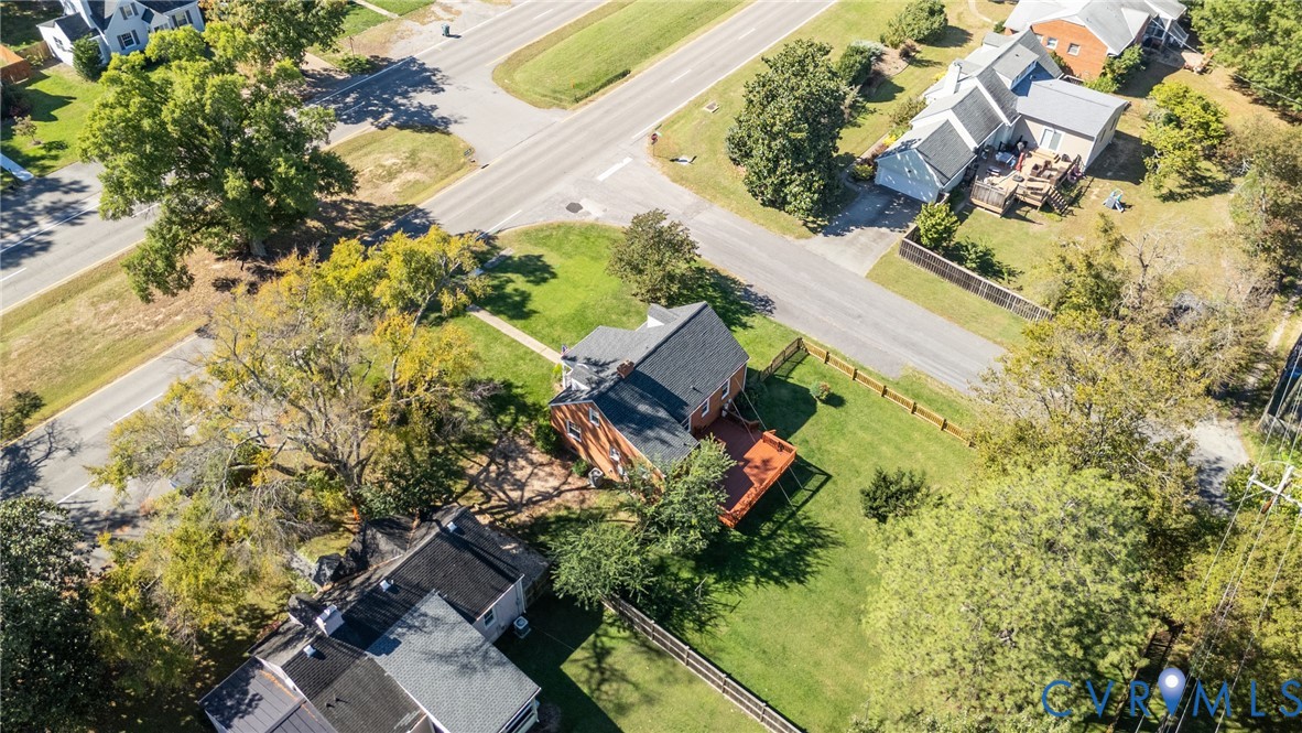 Aerial perspective of a detached property featuring a shingled roof, brick exterior, rear wood deck, and expansive grass lawn enclosed by wooden fencing