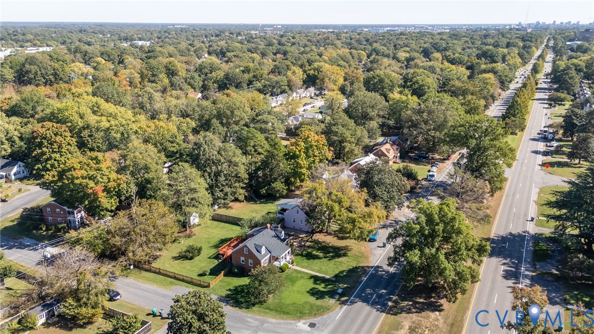 Aerial perspective of a corner lot property featuring a masonry exterior, a pitched roof, a paved driveway, and established surrounding tree canopy