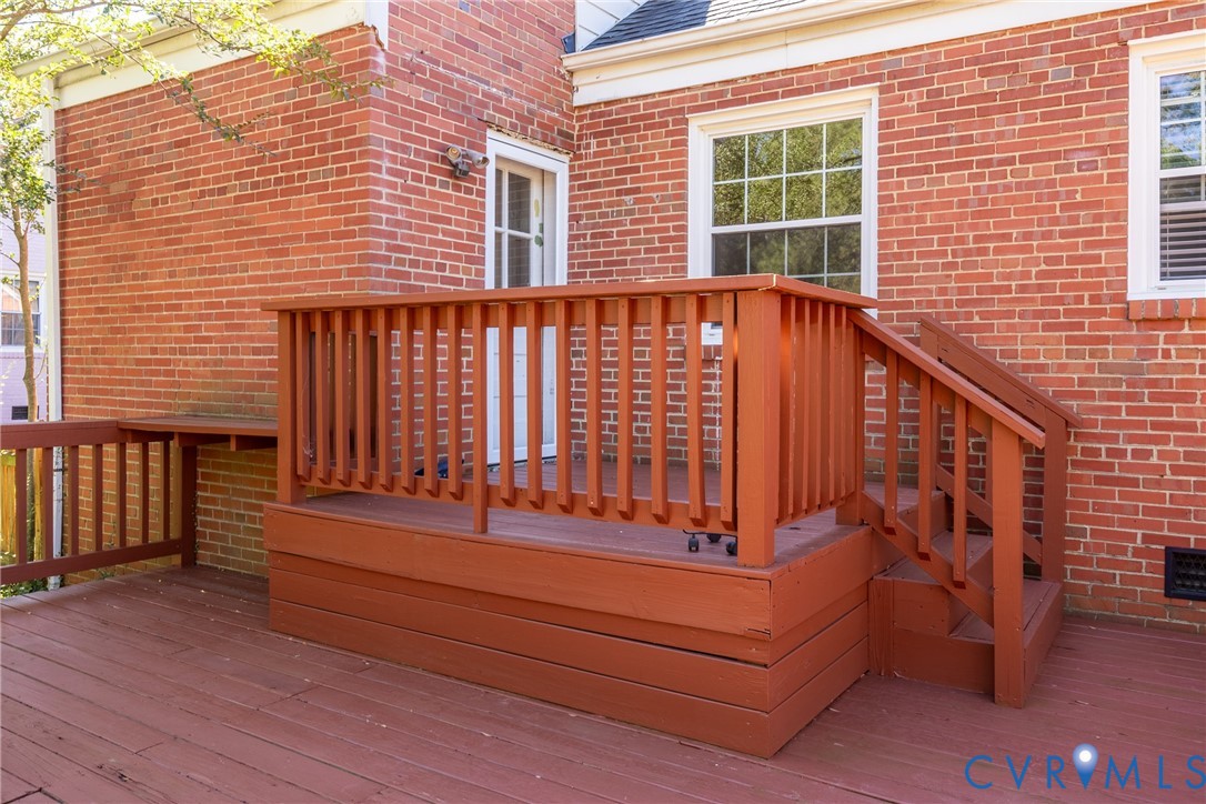 Exterior red brick facade featuring a raised wood-finish deck with integrated railing, matching staircase, and multi-pane window