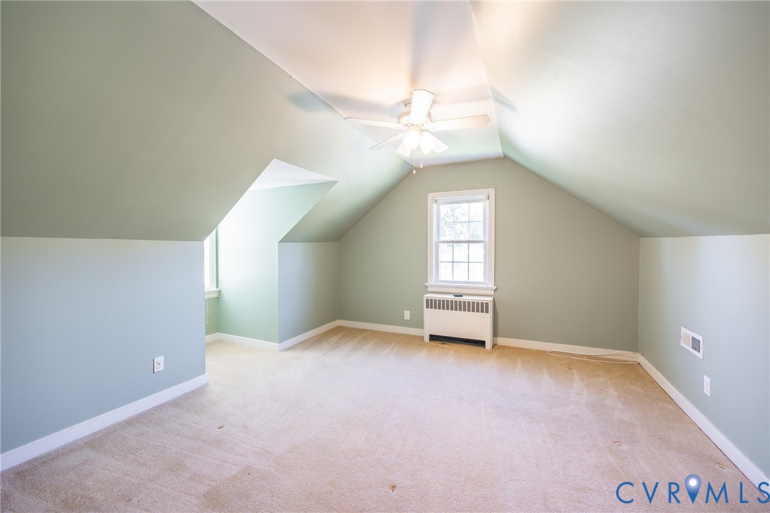 Vaulted ceiling with a centrally mounted ceiling fan, wall-to-wall carpeting, and a multi-pane window