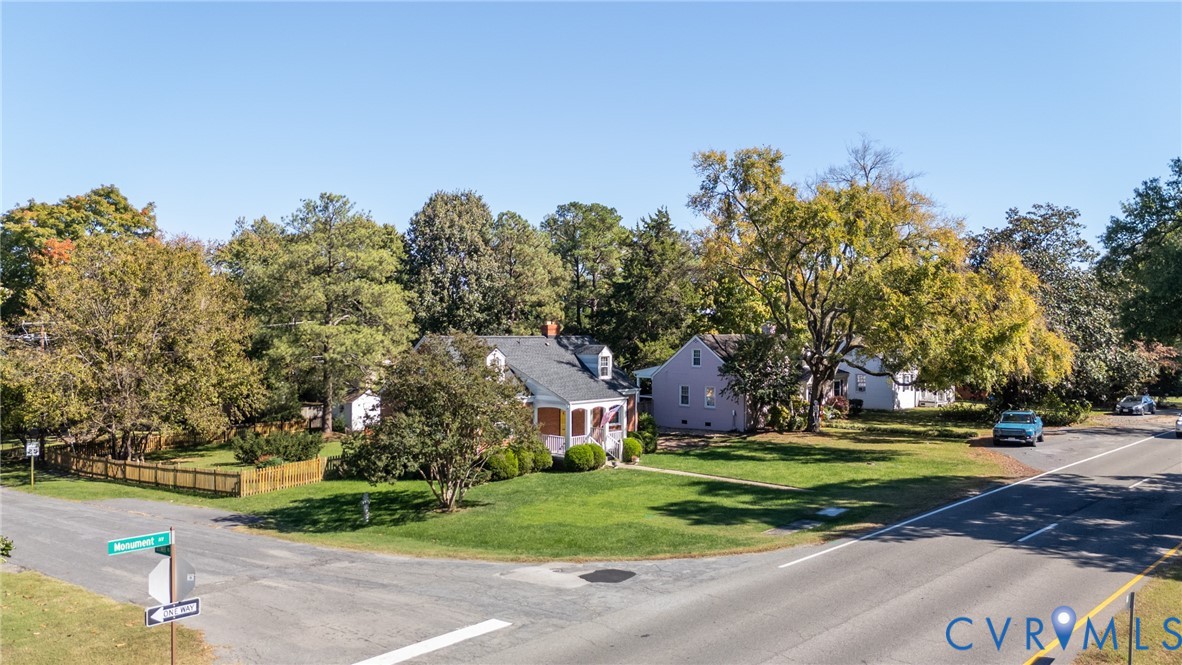 Corner lot exterior featuring a gable roof, covered front porch, and expansive lawn with mature trees and perimeter wood fencing
