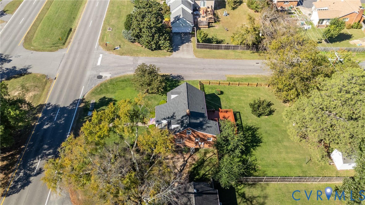 Aerial view of a brick exterior residence featuring a dark shingle roof, an elevated wooden deck, and a fenced yard with mature trees