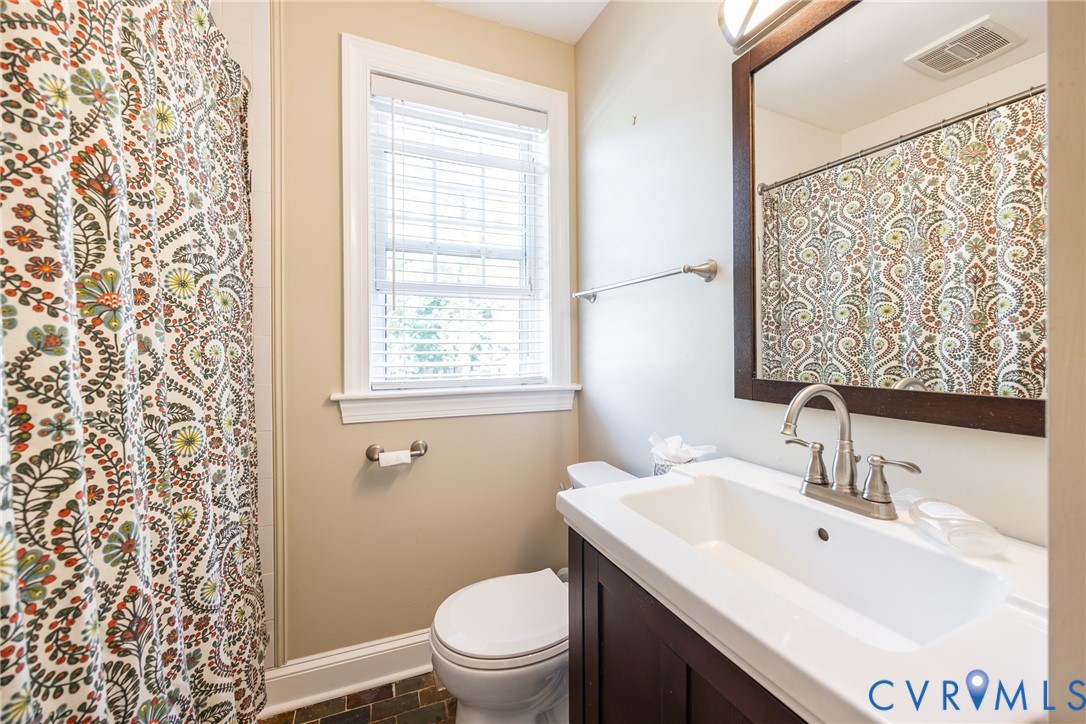 Bathroom featuring a dark wood vanity with a white integrated sink, high-arc brushed nickel faucet, framed wall mirror, and window with white slatted blinds