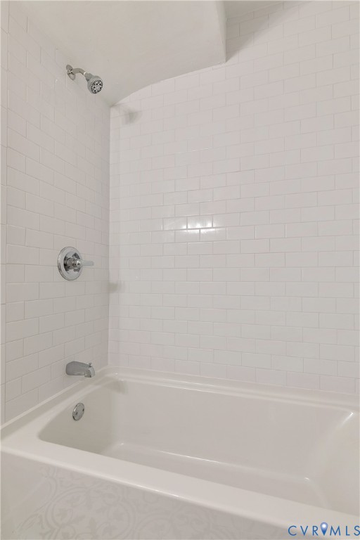 White subway tile shower surround featuring a full-sized bathtub with chrome fixtures