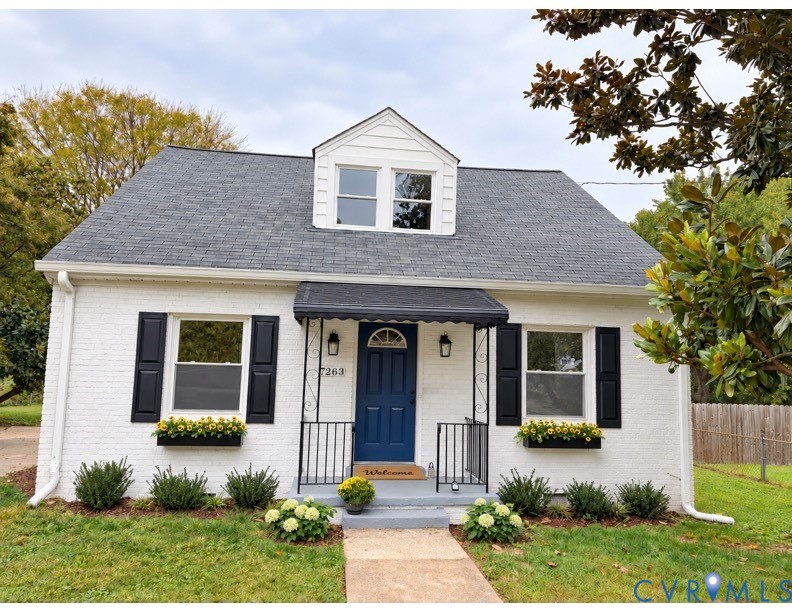 Painted brick exterior featuring a front-facing dormer, black shutters, metal door awning, and window-mounted planters