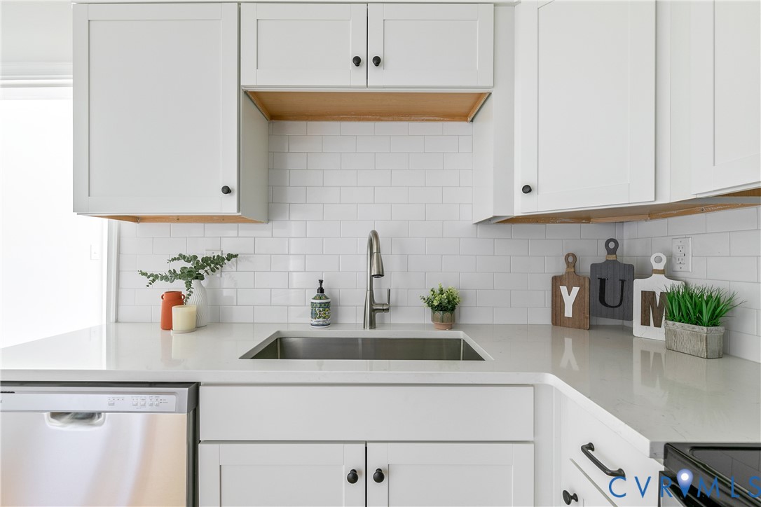Kitchen featuring white shaker-style cabinetry, a stainless steel sink with a gooseneck faucet, light-toned countertops, white subway tile backsplash, and a built-in stainless steel dishwasher