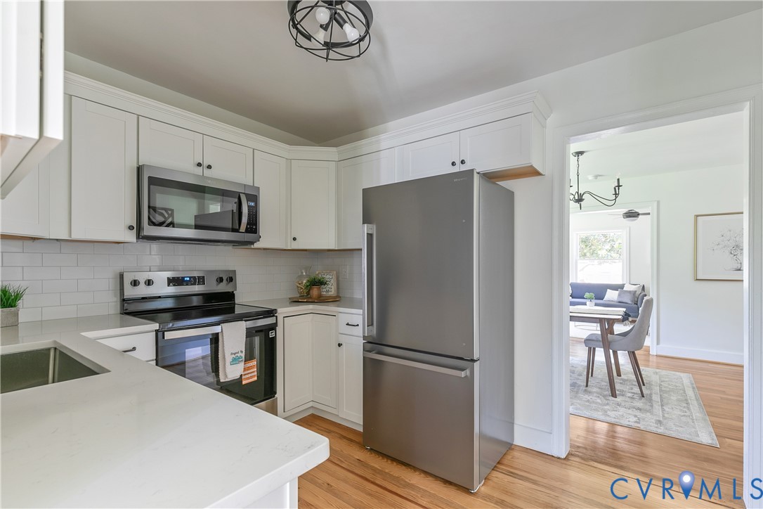 Contemporary kitchen featuring white cabinetry, stainless steel appliances, a subway tile backsplash, light-toned countertops, and wood-finish flooring