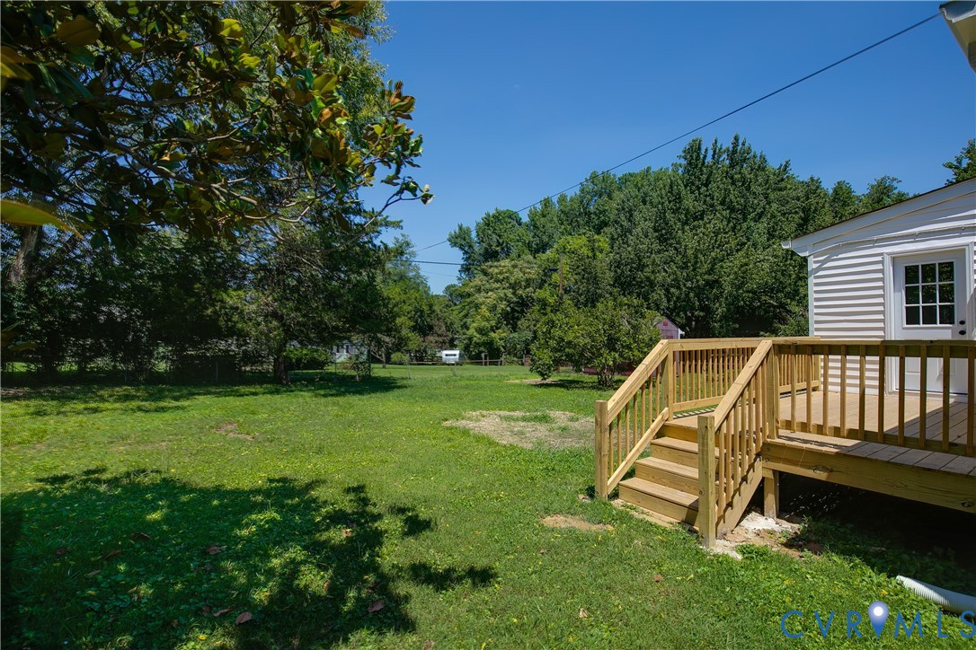 Expansive backyard featuring a new wood deck with stairs, white siding exterior, and mature trees surrounding the perimeter