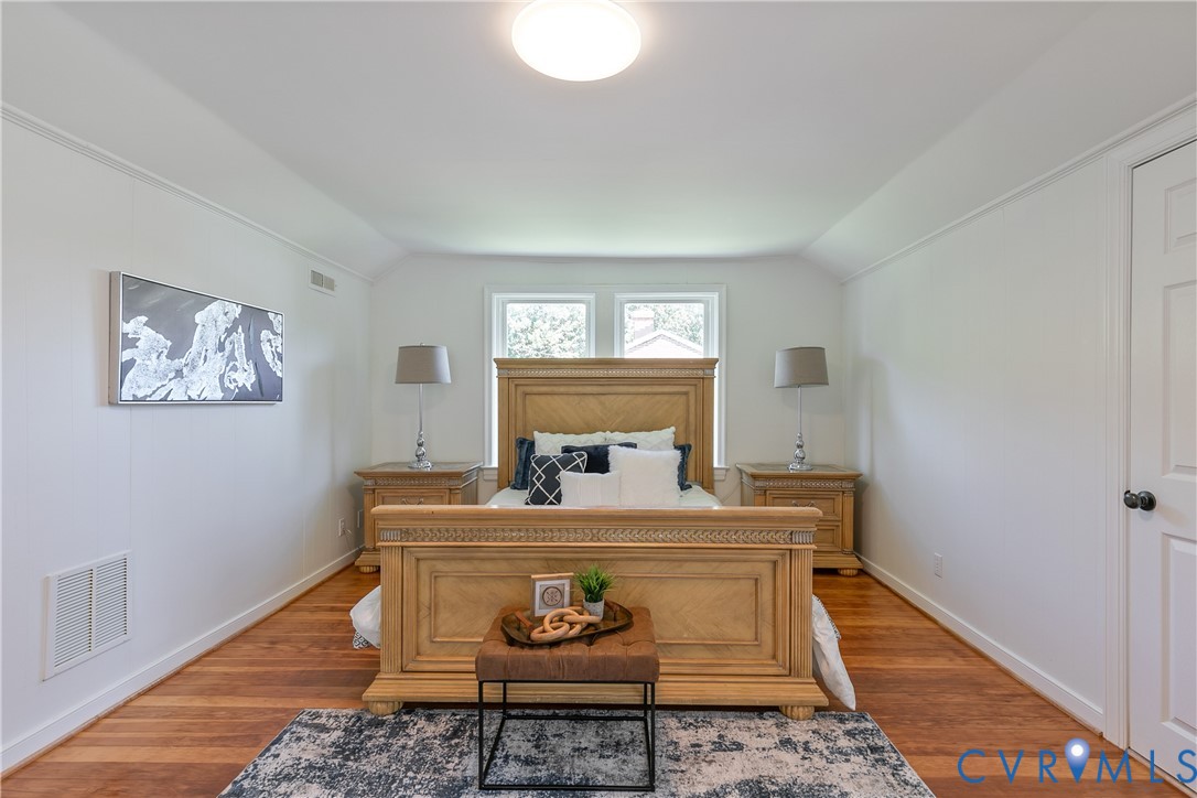Spacious bedroom featuring wood-finish flooring, white walls, and a pair of windows