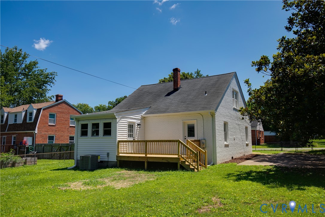 Rear exterior with a newly constructed wood deck, sunroom addition, white brick siding, and a gabled roof