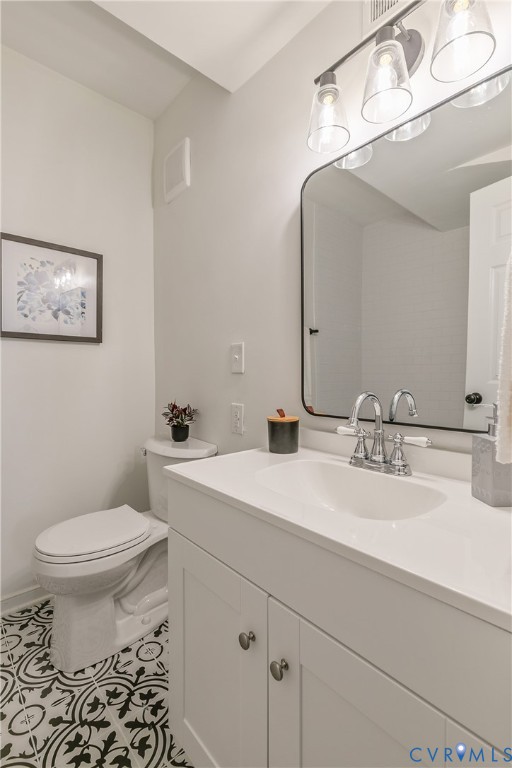 Bathroom featuring patterned floor tiles, a white vanity with panel cabinetry and silver-toned hardware, a white countertop with an integrated sink, a contemporary chrome faucet, and a rectangular mirror with a black frame