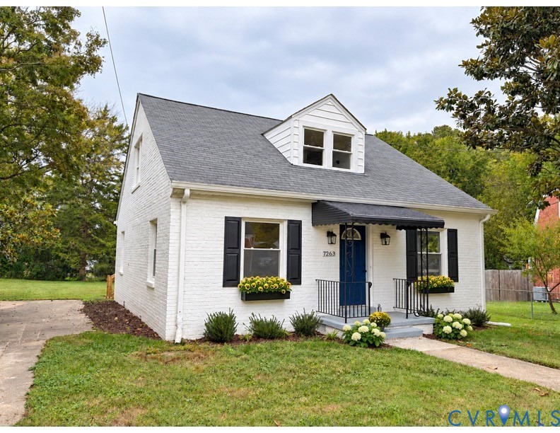 White brick exterior featuring a steep gabled roof, prominent front-facing dormer, contrasting black window shutters, and a metal door awning