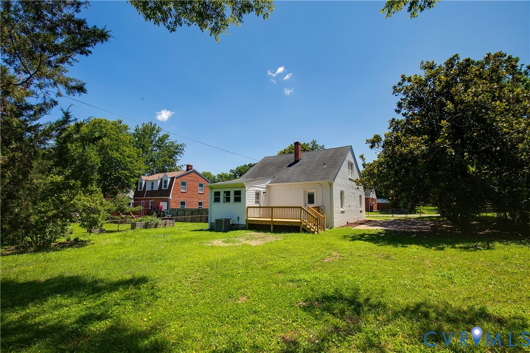 Expansive rear yard featuring a white-painted brick exterior, a newly constructed wood deck, a white sunroom addition, and mature perimeter trees
