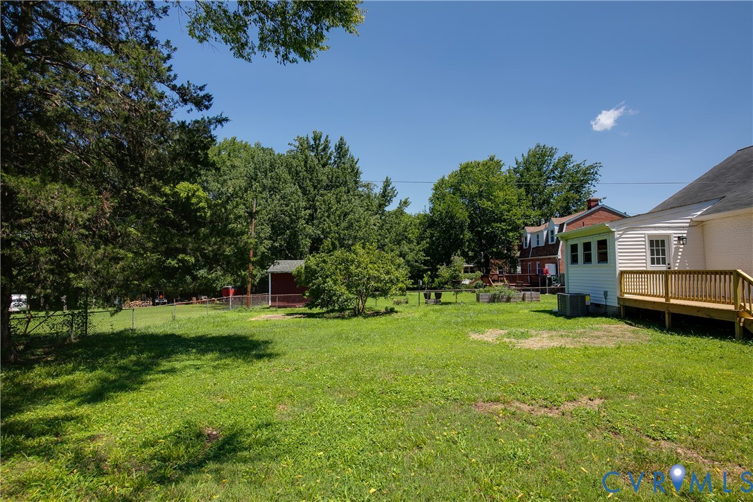 Expansive green lawn with mature trees, a wooden deck, and a detached red shed