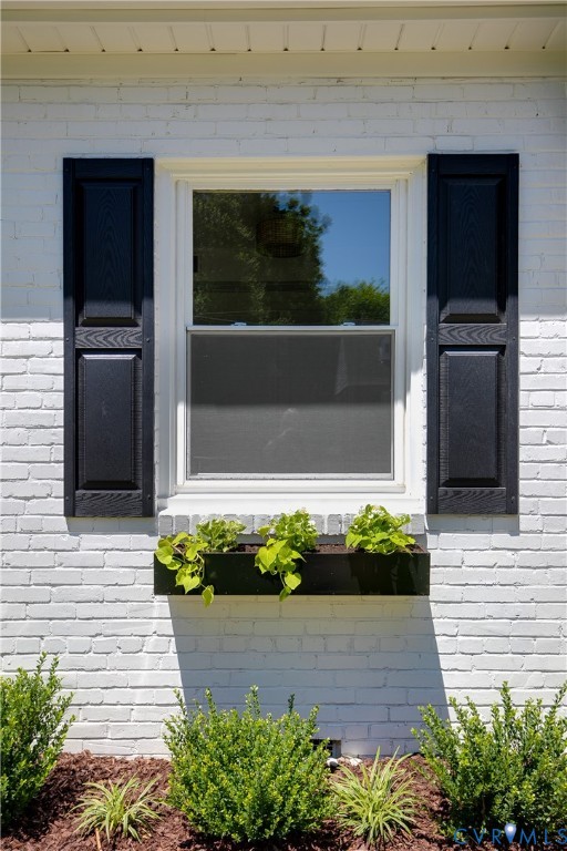 White painted brick exterior featuring a double-hung window with white framing, black louvered shutters, and a black window box with plantings