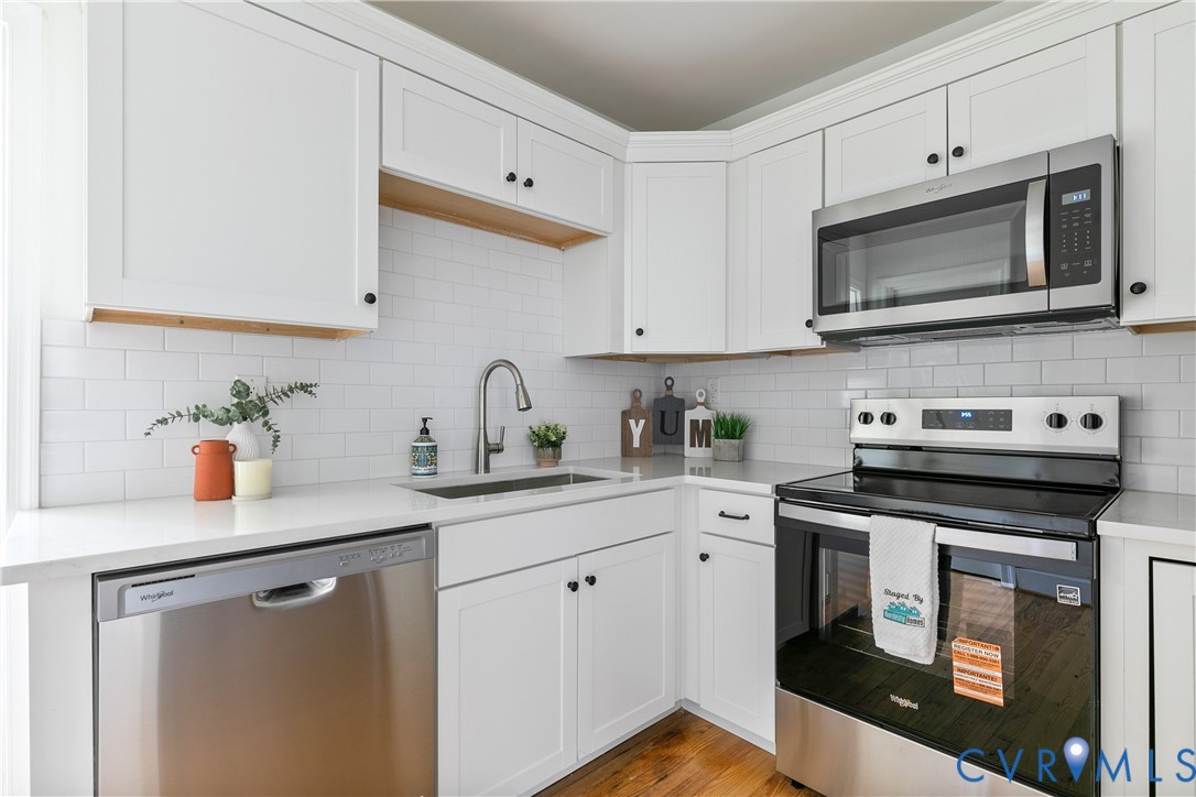 Modern kitchen featuring white shaker cabinetry, stainless steel appliances, a subway tile backsplash, light countertops, and wood-finish flooring
