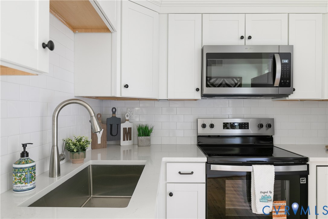 Modern kitchen featuring white shaker cabinetry with dark hardware, stainless steel appliances, a subway tile backsplash, a gooseneck faucet, and light-toned countertops