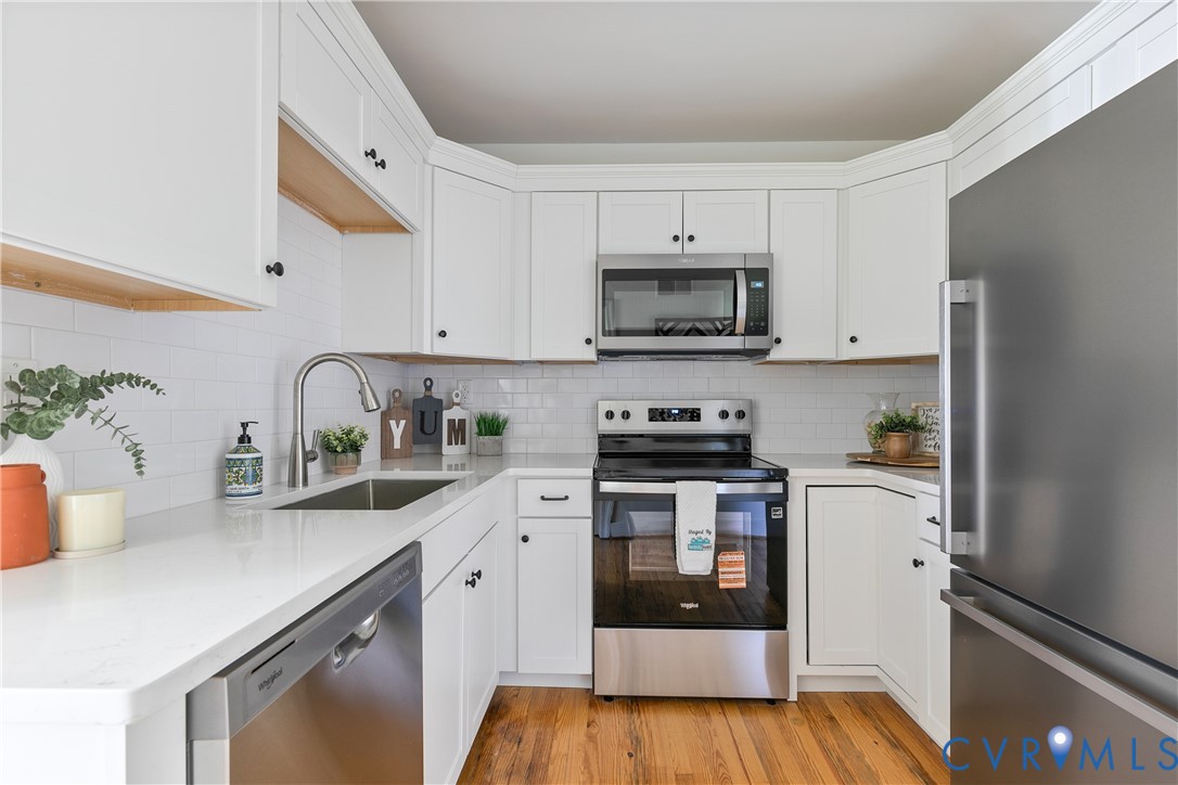 Kitchen featuring white shaker cabinetry, white subway tile backsplash, stainless steel appliances, and wood-finish flooring