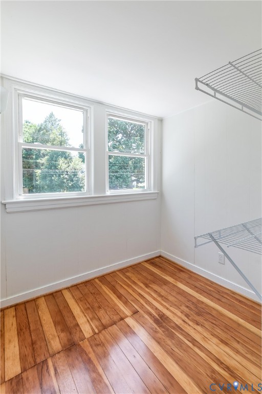 Room featuring two windows, wood-finish flooring, white walls, and built-in wire shelving