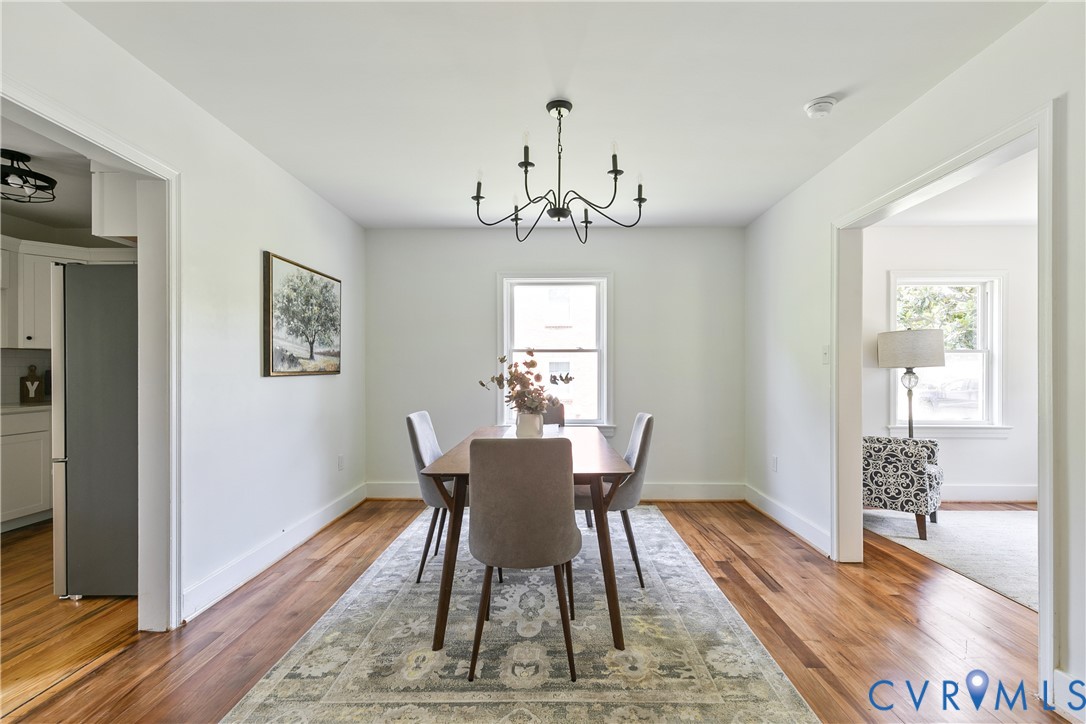 Dining space featuring wood-finish flooring, a black iron chandelier, a window with natural light, and white baseboards