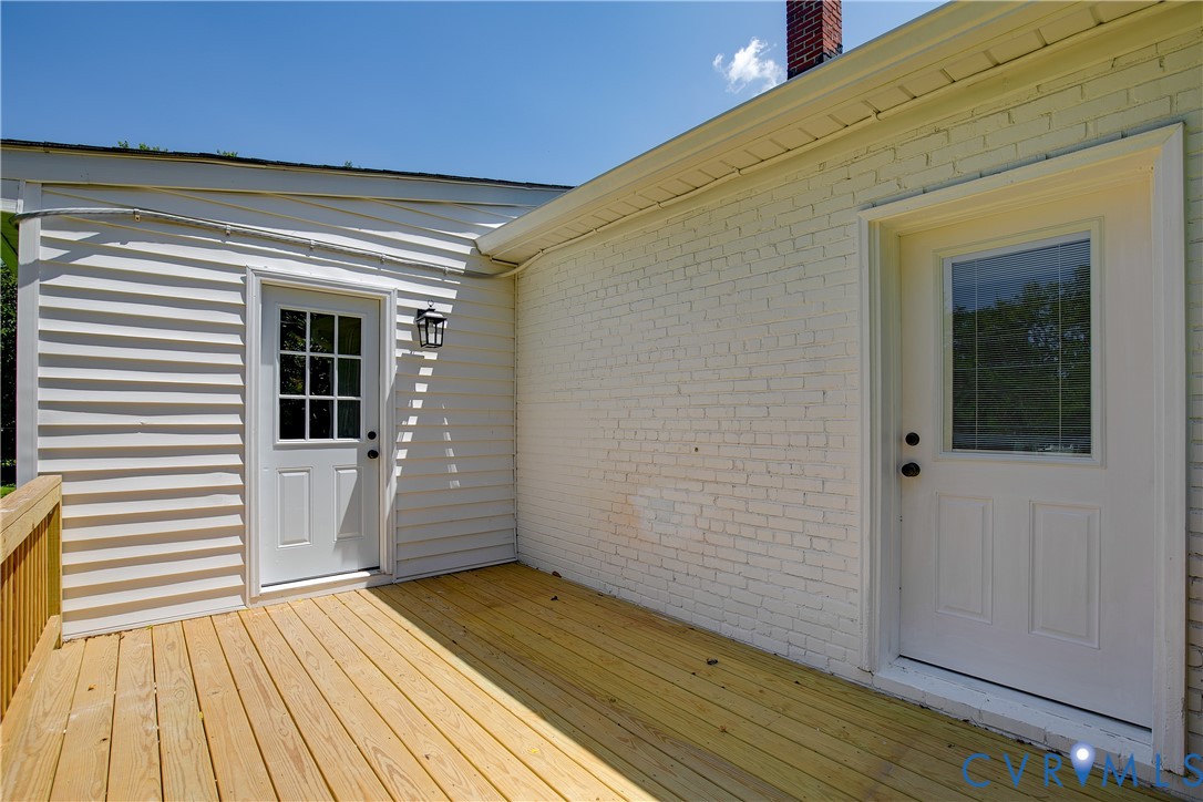 Expansive wooden deck with natural finish, featuring two white entry doors with glass lites, a white brick exterior, and white vinyl siding