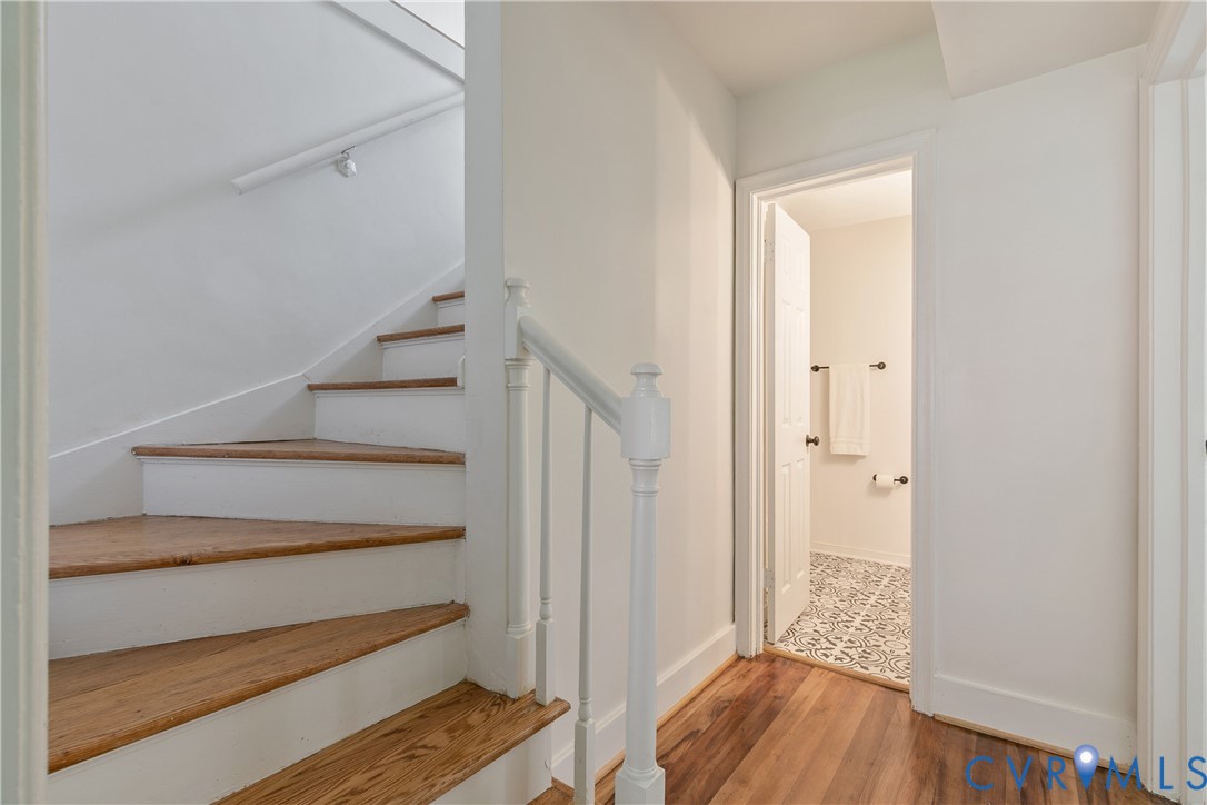 Hardwood flooring extending from the hallway into the visible room, white staircase with wood treads and white risers, white painted balusters, and a white handrail