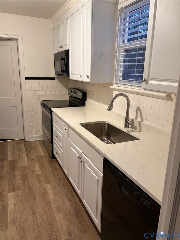 Kitchen featuring white cabinetry, quartz countertops, subway tile backsplash with a decorative black accent border, stainless steel undermount sink, and wood-finish flooring