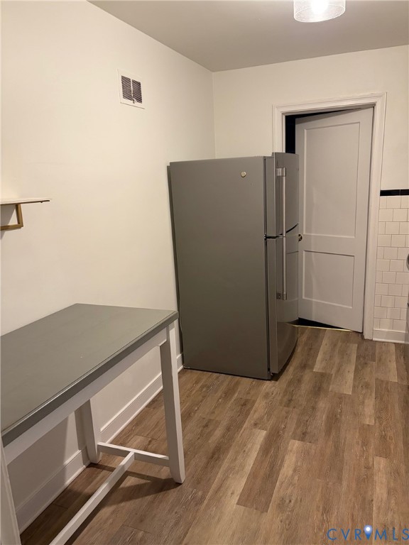 Wood-finish flooring, stainless steel refrigerator, white subway tile backsplash with black decorative accent, and recessed ceiling lighting