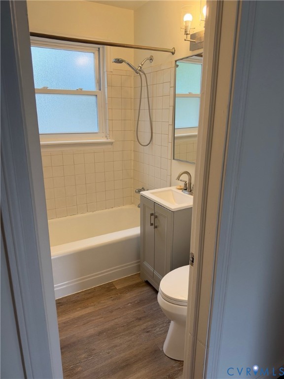 Bathroom featuring a wood-finish floor, white porcelain tub with square tile surround, single-basin vanity, and a rectangular wall-mounted mirror
